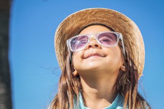 Chica protegiendo su visión con gafas de sol y sombrero.