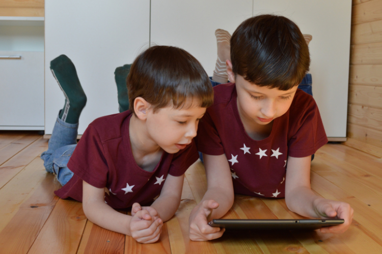 Two children lying on the floor using a tablet, illustrating screen time habits and potential impact on children’s vision