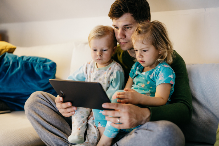Father and two young children using a tablet together at home, illustrating screen time and children’s vision