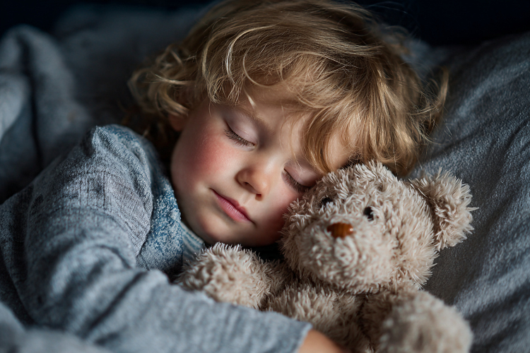 Child sleeping peacefully with a teddy bear, highlighting the importance of sleep for visual development