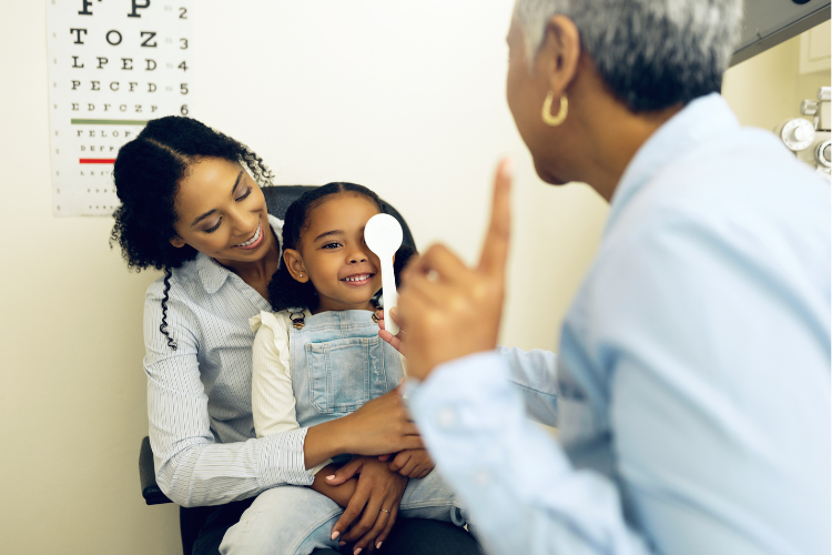 Child having an eye exam with her mother and an eye care professional.